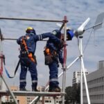 Operarios en estructura metálica junto a un aerogenerador pequeño