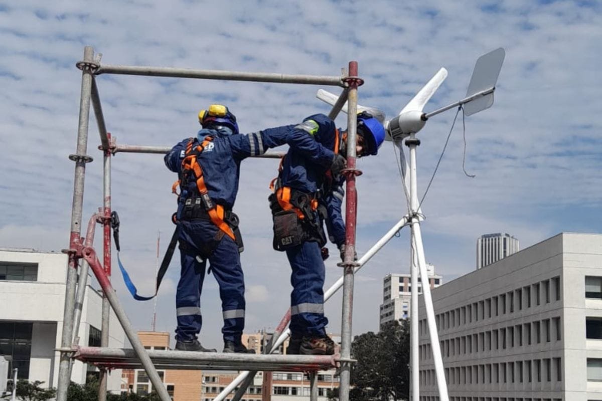 Operarios en estructura metálica junto a un aerogenerador pequeño